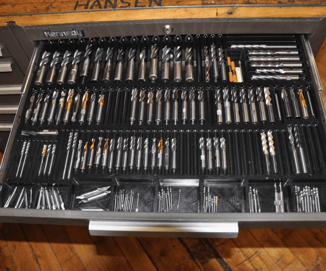 Drill bits, assorted twist drills and end mills in a metal organizer.