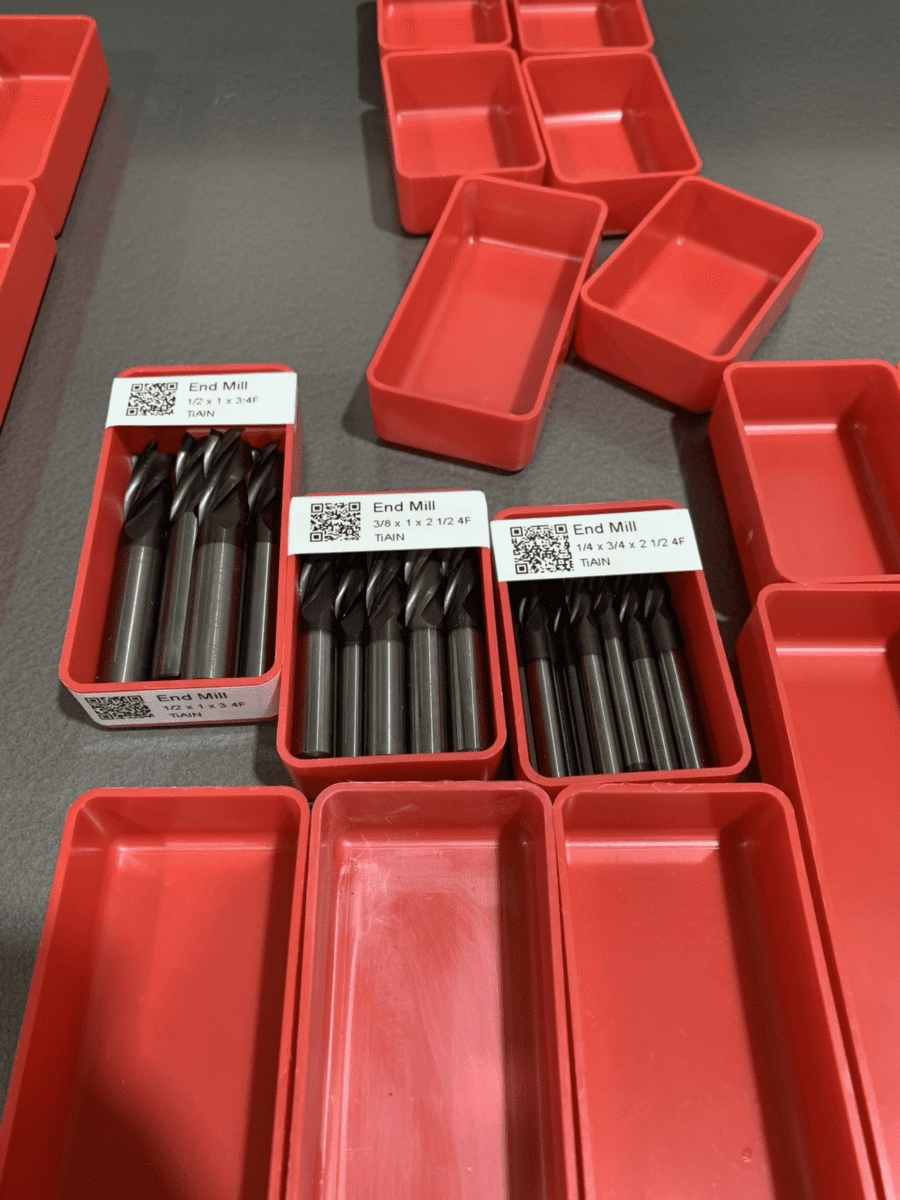 Red plastic containers filled with metal End Mill drill bits, labeled and featuring QR codes.
