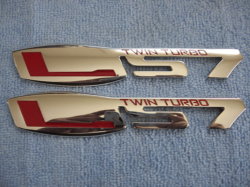 Shiny metal parts with "Twin Turbo" in red on a blue fabric background.