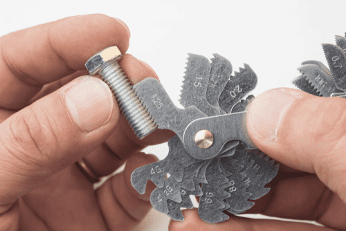 A hand holding a small metal tool with serrated edges and numbers on it, against a white background.